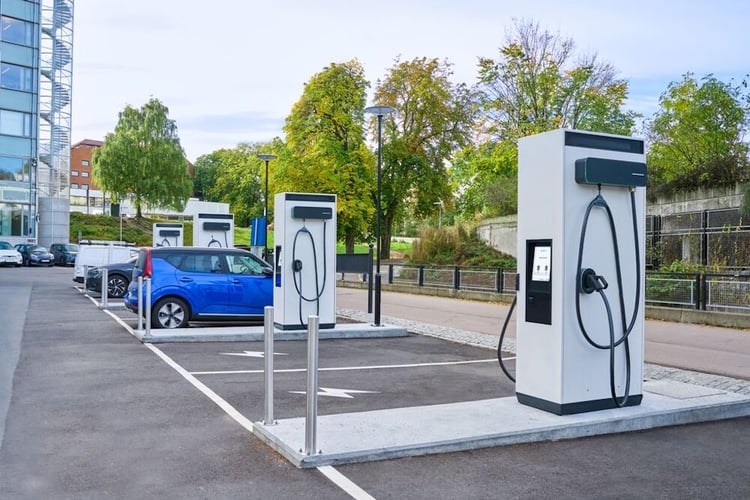 A parking lot at a workplace location with 4 EVBox Troniq Modular DC fast charging stations installed and a blue car charging.