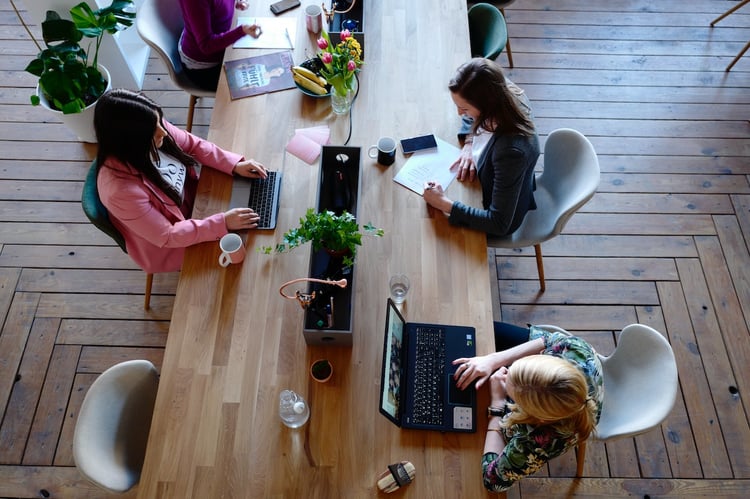 Three women working on a long wooden desk. 