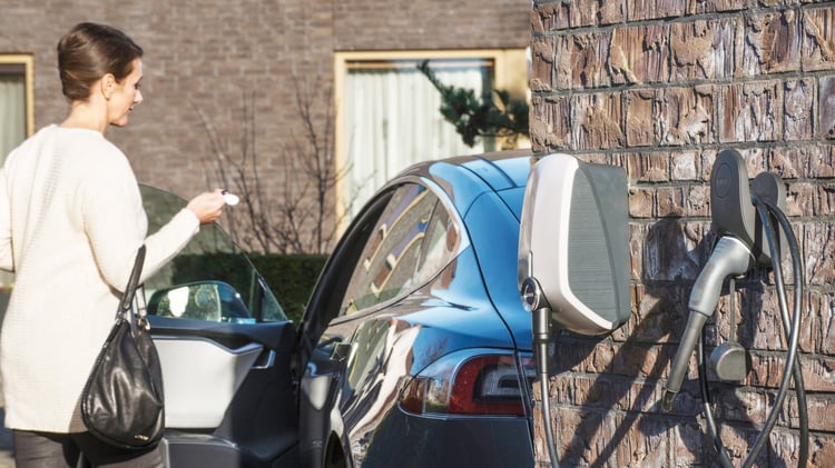 Een man die de connector van zijn elektrische auto sluit en een oplader vasthoudt. 