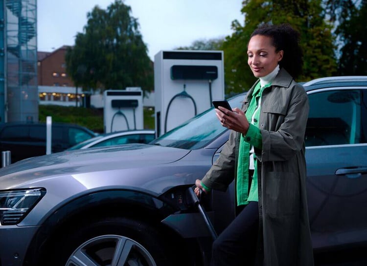 A lady fast charging her vehicle at an EVBox Troniq Modular DC fast charging station while conveniently paying via her smartphone.