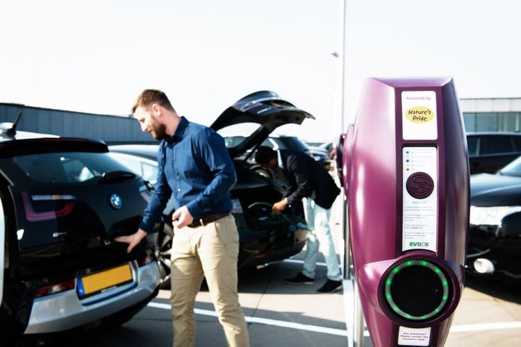 EVBox BusinessLine charging station personalized with a corporate branding. In the background, there is a businessman opening the truck of his car.