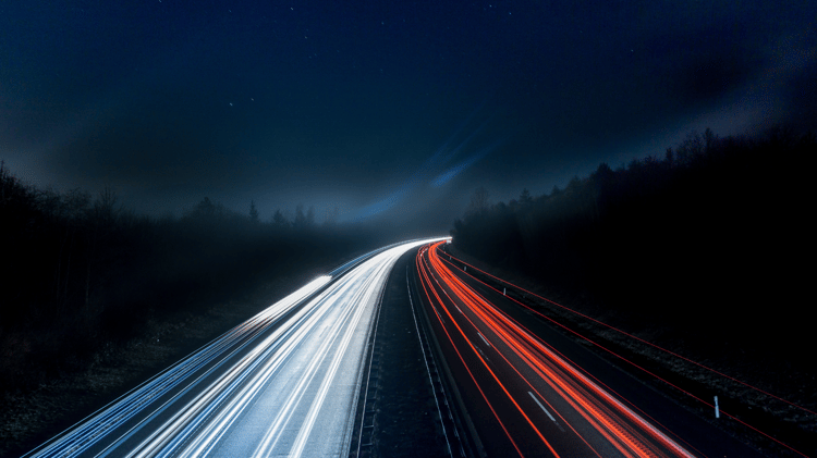 A stream of lights coming from vehicles on the road at night taken by a camara with a slowed shutter speed setting