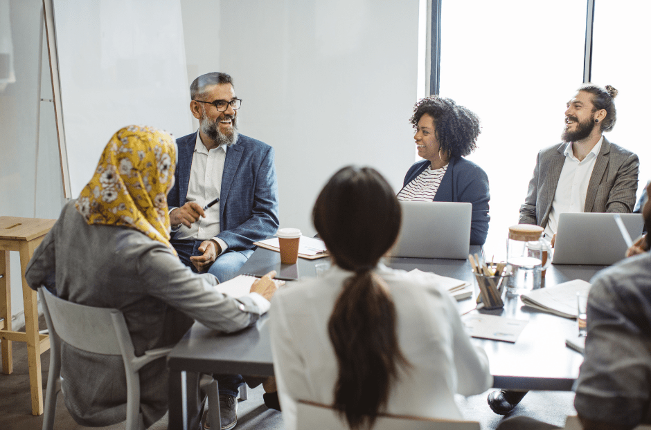 People sitting around a table in an office, laughing in a meeting.