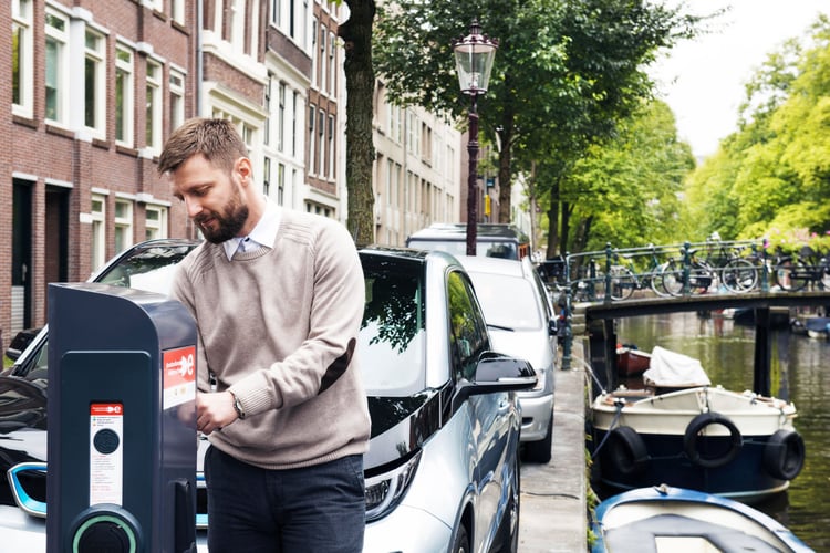 Un homme habillé de manière décontractée utilise une borne de recharge publique dans la ville d'Amsterdam.
