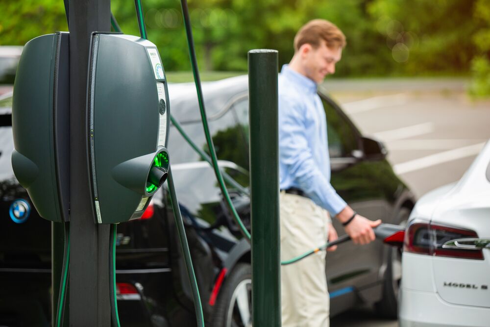 A black EVBox BusinessLine is in the foreground whilst a man in white trousers and a blue smart shirt charges his white electric car in the background.