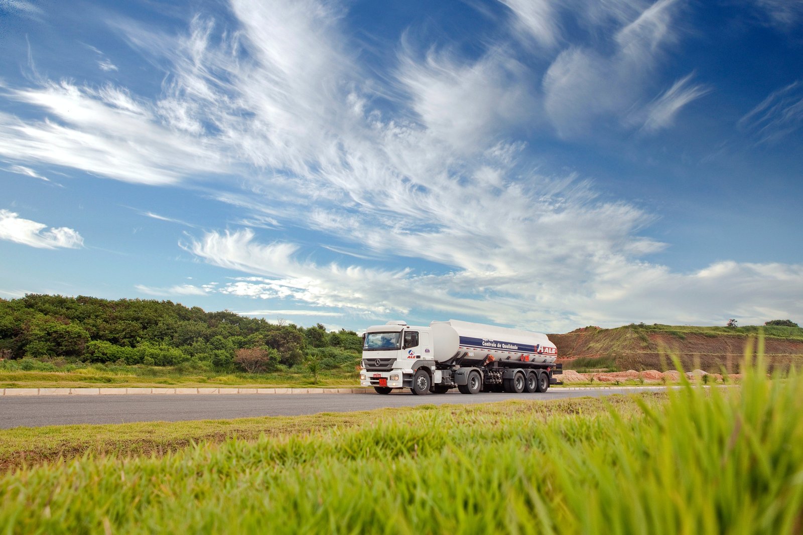 A truck carrying fuel under a blue sky scattered with clouds.