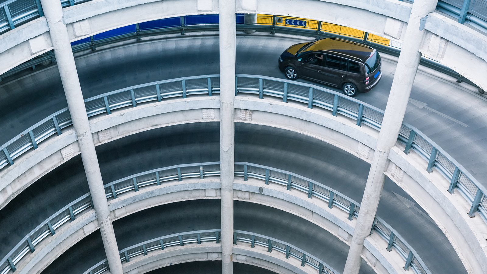 A three story parking lot with an electric vehicle descending from the top. 