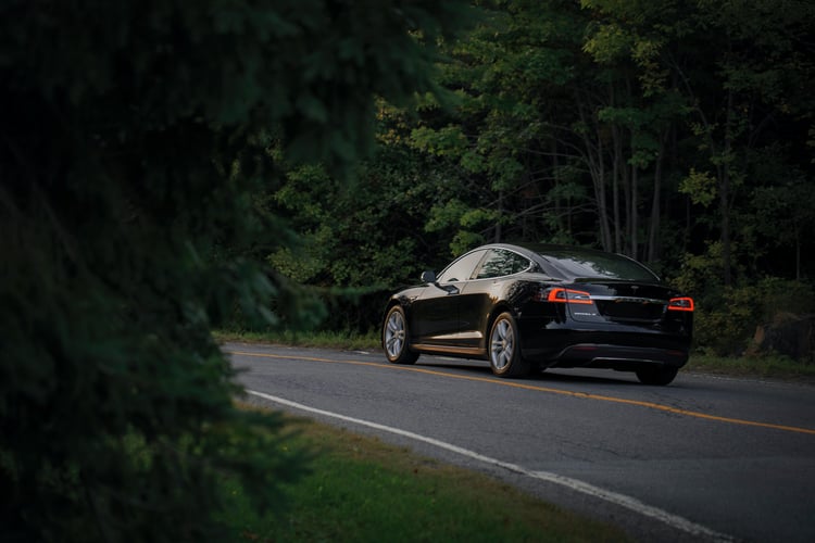 Black car driving down road surrounded by trees.