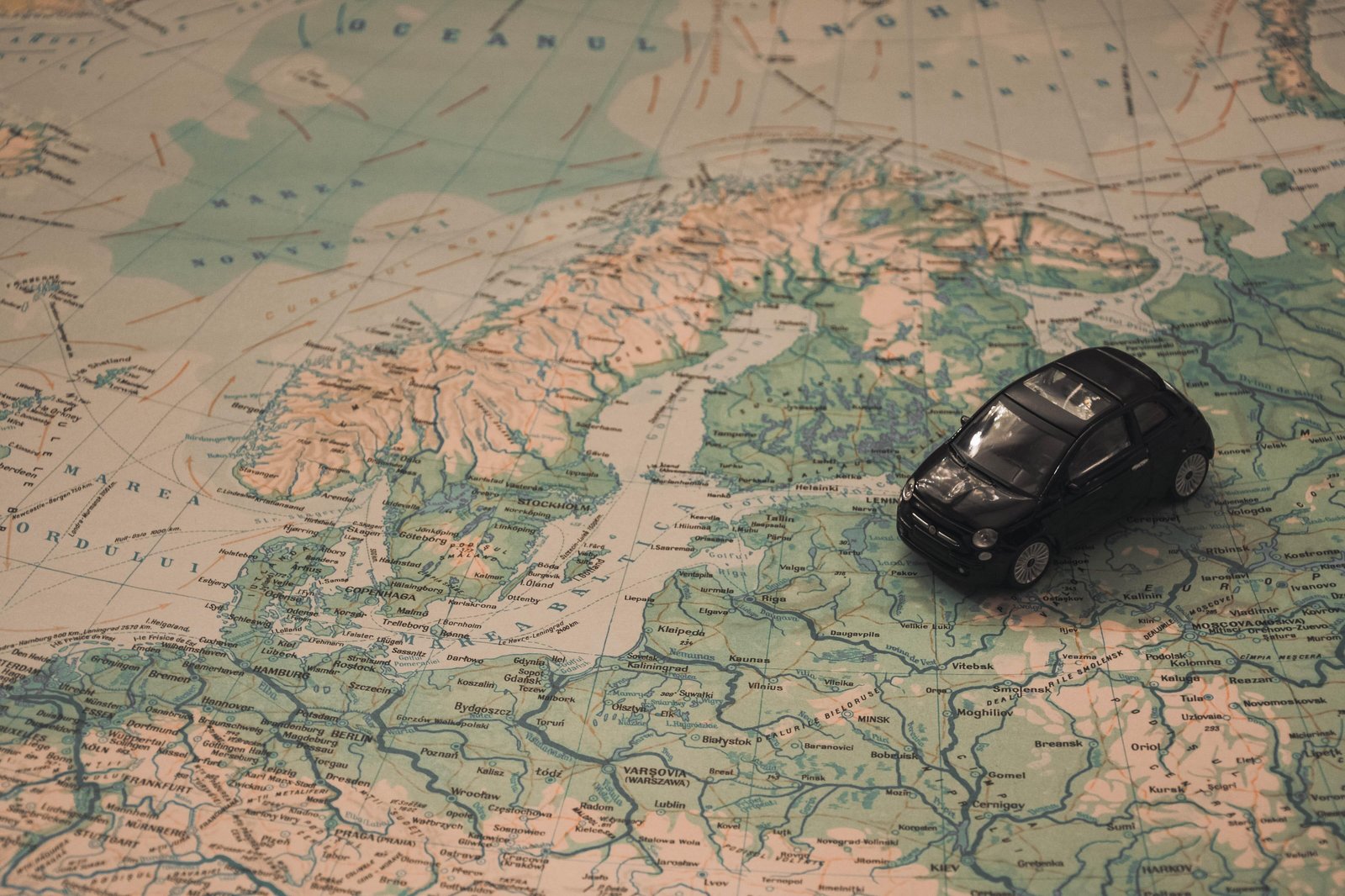 A black miniature toy car model placed on top of a detailed map of Europe.