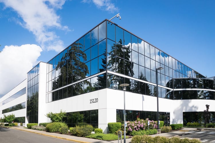 An large office building basking in the sun during springtime in front of a parking area.