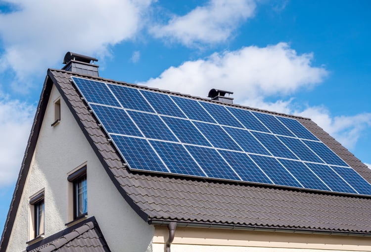 A series of solar panels installed on the sloping roof of an independent house on a sunny day.