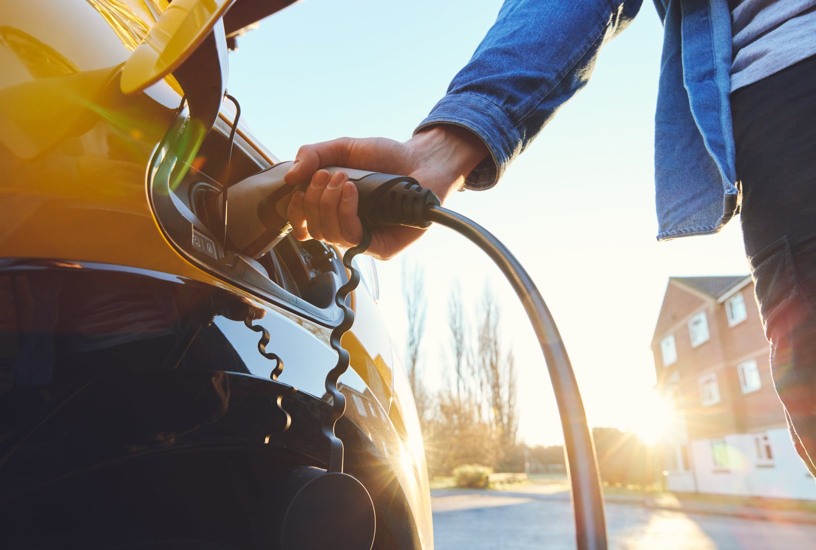 a close up from someone who plugs in an electric car charging cable into an electric vehicle at a residential setting during sunset.