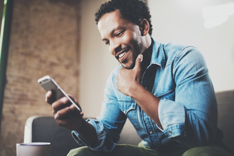 A smiling man is looking at his smartphone while checking EV charging data and insights of his electric car.